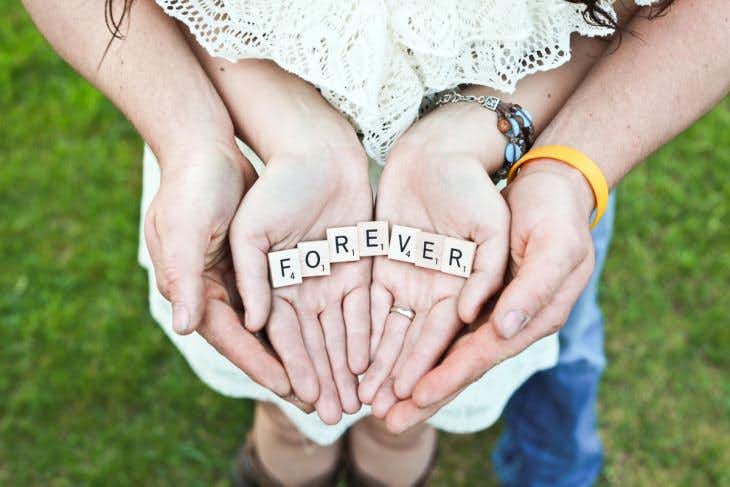 Hands holding letter tiles spelling 'forever'