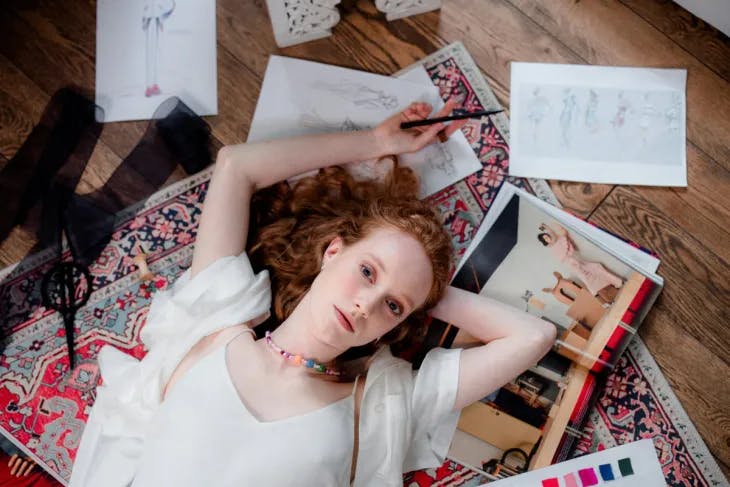 Fashion designer lying on the floor surrounded by her sketches