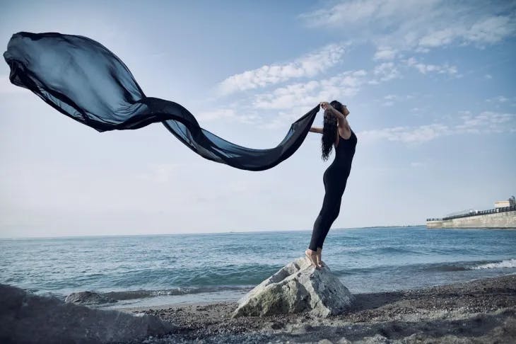 Woman standing on a beach rock with billowing fabric behind her