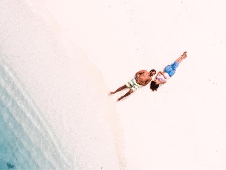 Two people lying down together on the shore