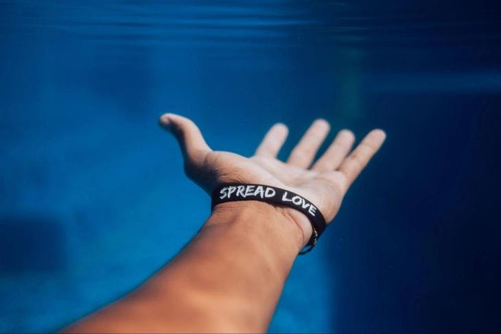 Hand underwater wearing a band that reads 'Spread Love'