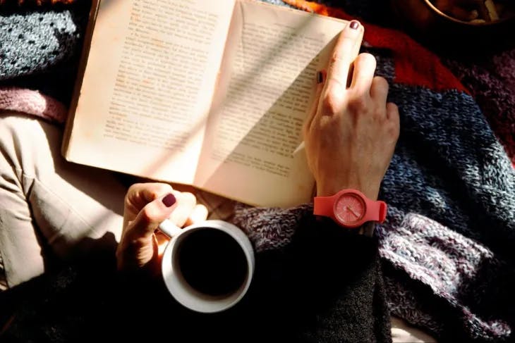 A woman reading a book while holding a cup of coffee