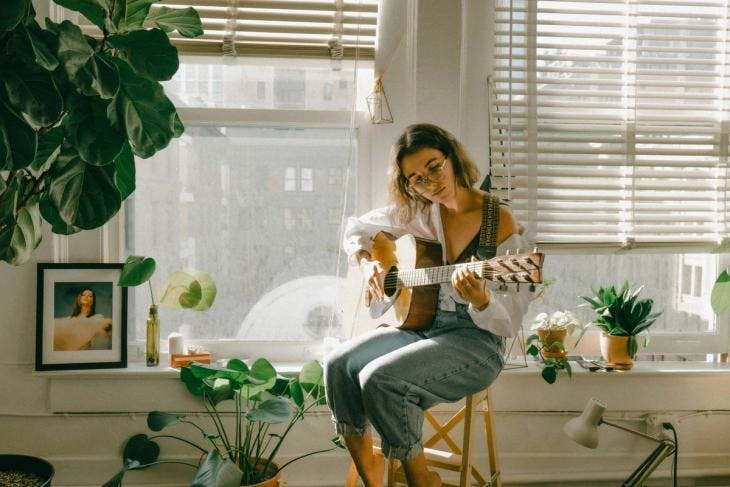Girl playing guitar in her room by the window
