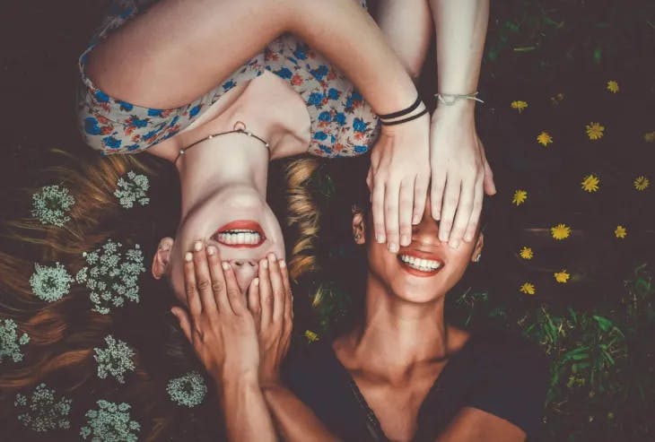 Two girls lying down, smiling as they cover each other's eyes