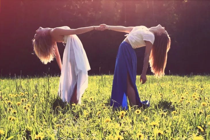 Two girls holding hands and leaning backwards in a vibrant flower field