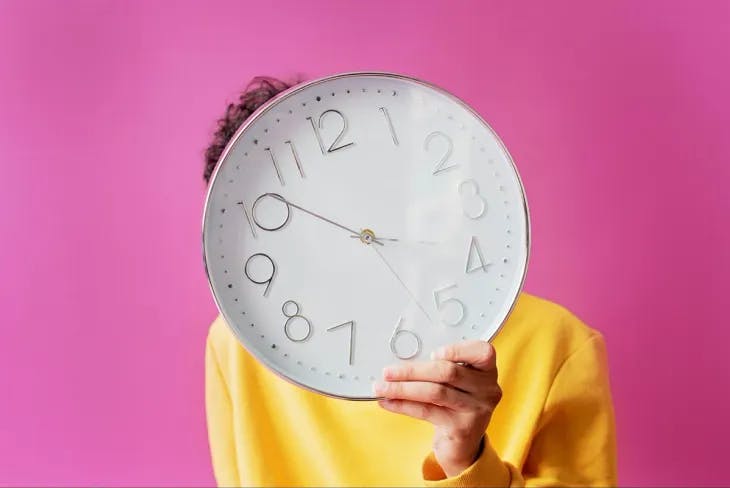 A man holding up a big clock in front of his head