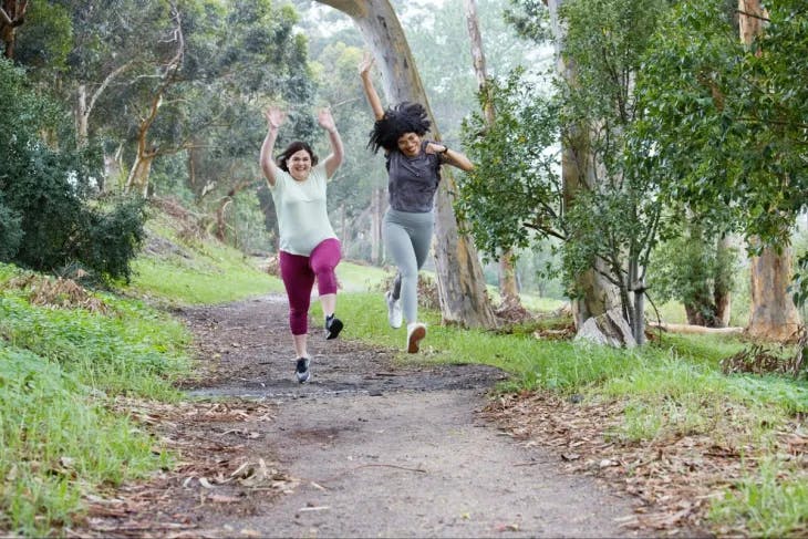 Two girls happily jumping on a park walkway