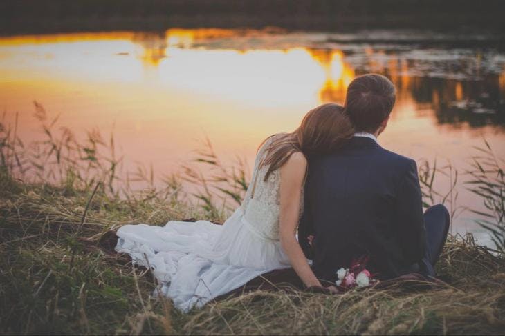 a newly wedded couple sitting in front of a lake
