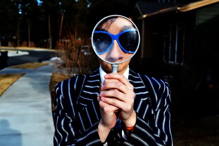 Man wearing blue-framed sunglasses, looking through a magnifying glass