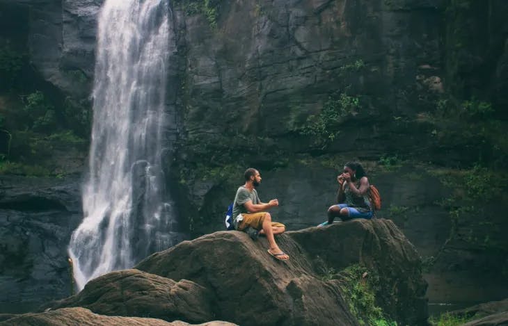 A couple sitting on a rock next to a waterfall